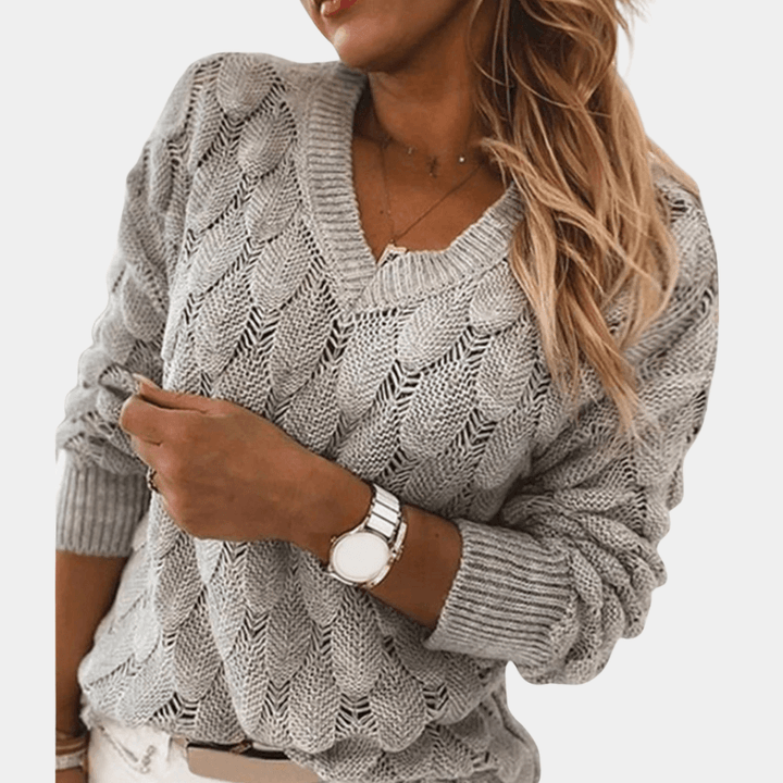 Grijze gebreide damestrui met V-hals, gedragen door model. Modieuze, comfortabele trui voor herfst en winter. Perfect voor casual outfits.