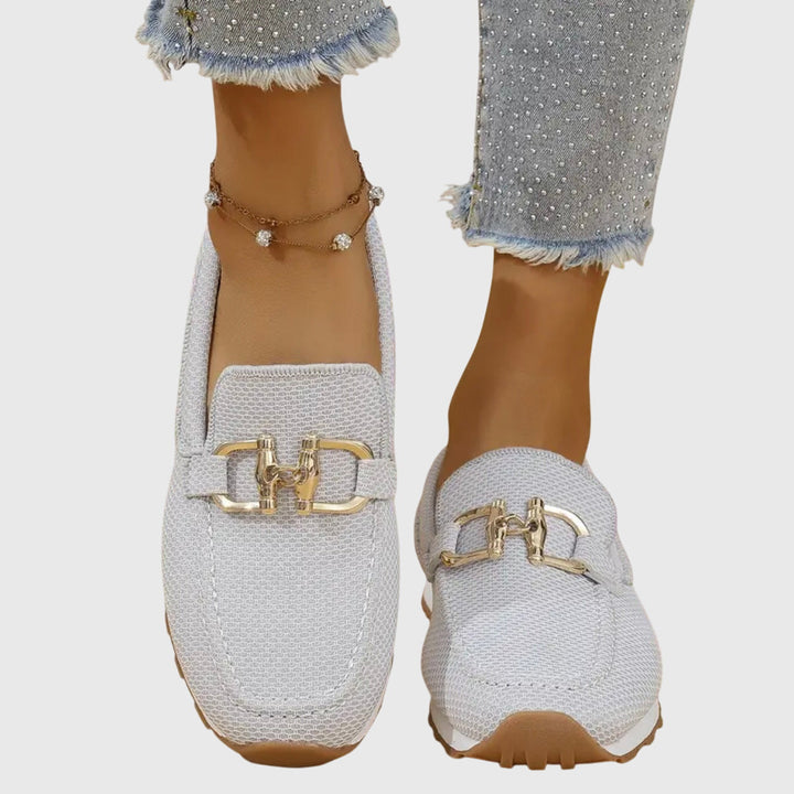 Zijkant van dames loafers met stevige plateauzool en glanzende gouden gesp, een modieus detail.