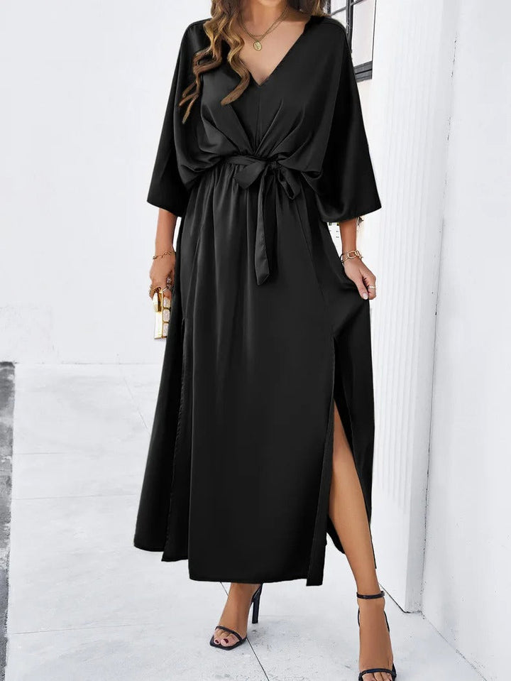 Prachtige dames jurk met diepe V-hals, vloeiende vleermuismouw en elegante strikceintuur. Ideale avondkleding.