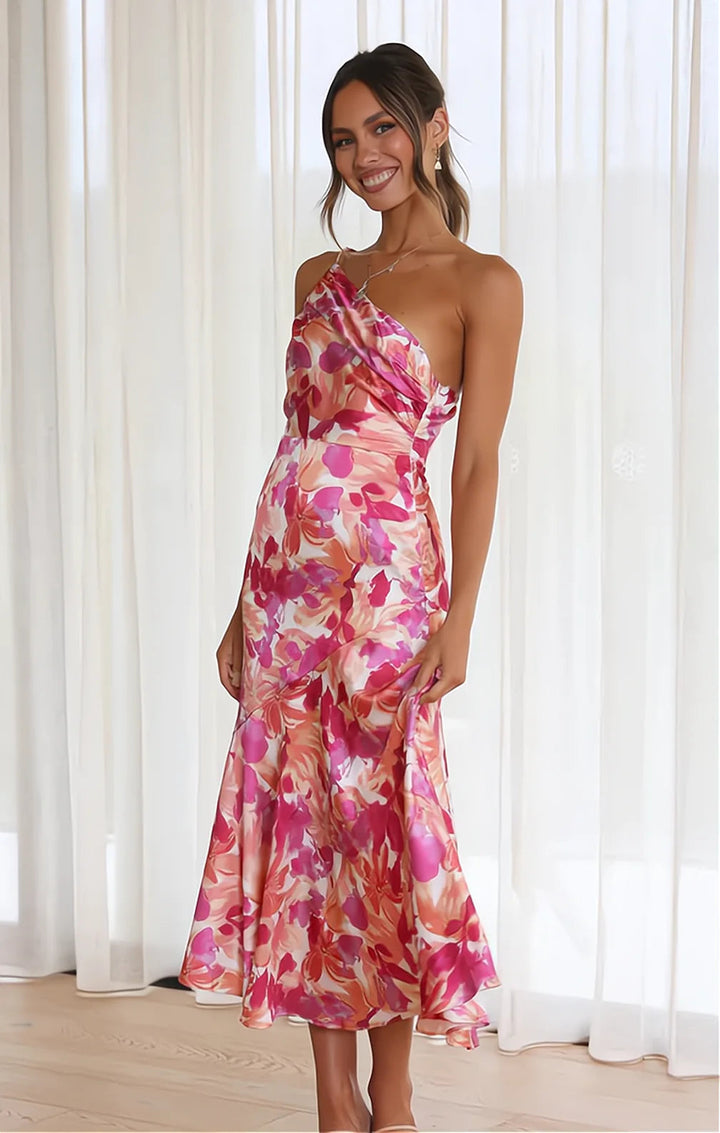 Model toont de unieke eenschouderlijn van de feestelijke dames midi jurk met kleurrijke bloemen.