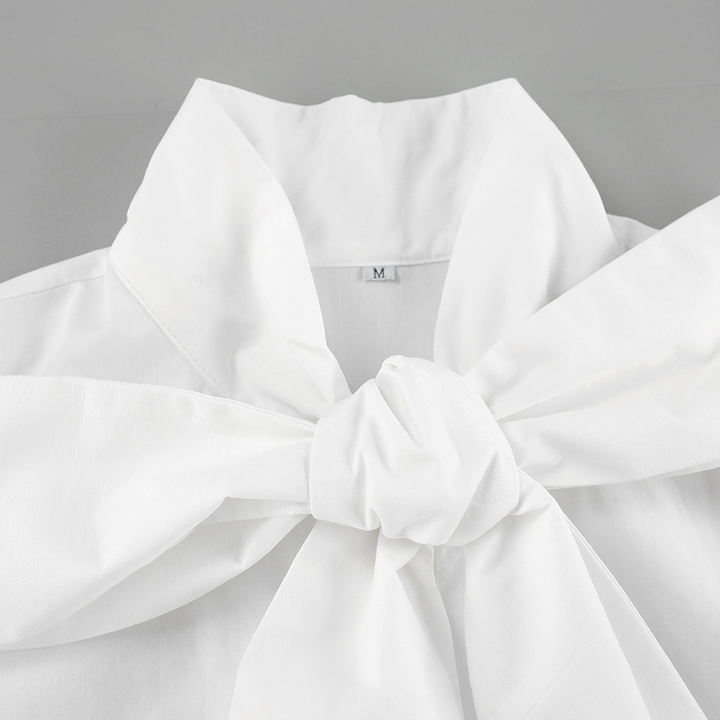 Detail van de elegante strik op het witte dames overhemd, voor een klassieke en verfijnde uitstraling.
