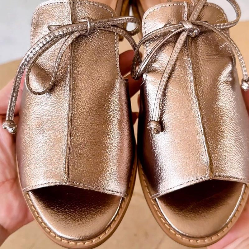 Detail van platte dames sandaal met strikbandje en open neus. Trendy metaallook zomersandaal, perfect voor damesmode.