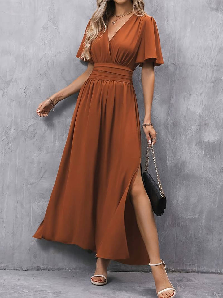 Vrouw draagt een lange karamel damesjurk met split, ideaal als zomerjurk of elegante feestjurk.