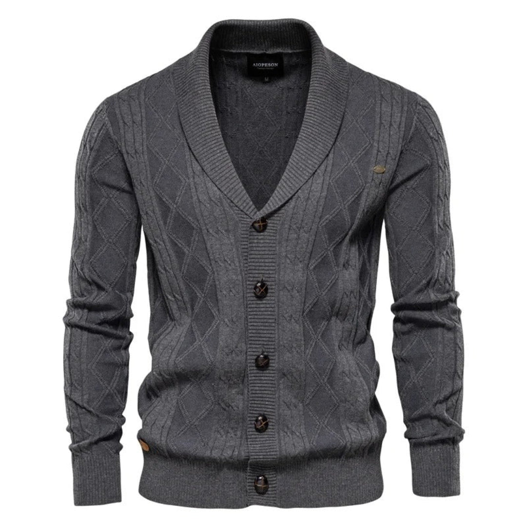 Detail van gebreid herenvest met sjaalkraag, knoopsluiting en verfijnd ruitpatroon. Geschikt voor heren kleding.
