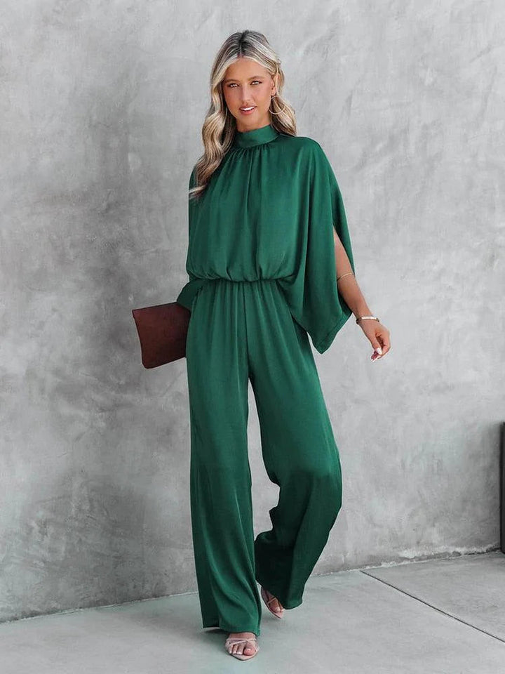 Groene dames jumpsuit met elegante capemouwen en flatterende tailleband, ideaal voor feestkleding.