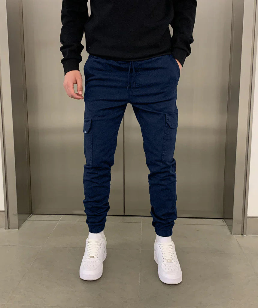 Man draagt stijlvolle slim-fit heren cargobroek met zakken, gecombineerd met casual outfit.