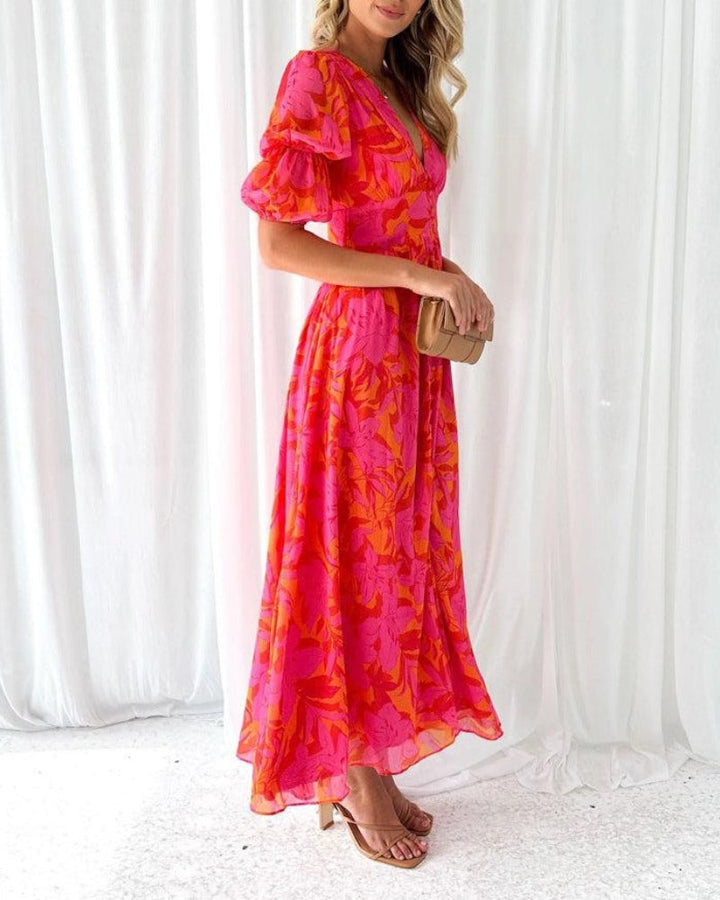 Lange roze damesjurk met exotische tropische print, diepe V-hals en trendy pofmouwen. Comfortabele zomer maxi jurk.